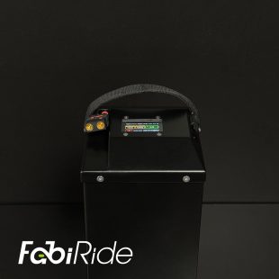 Juodas elektrinis krosinis motociklas su geltonais akcentais žalios sienos fone.